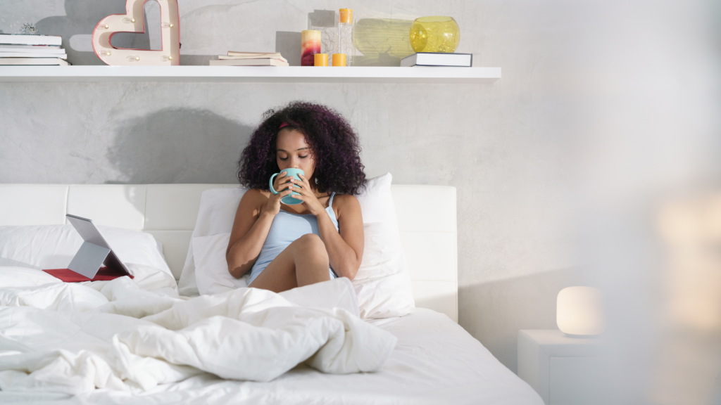 woman in bed drinking from a mug watching her tablet